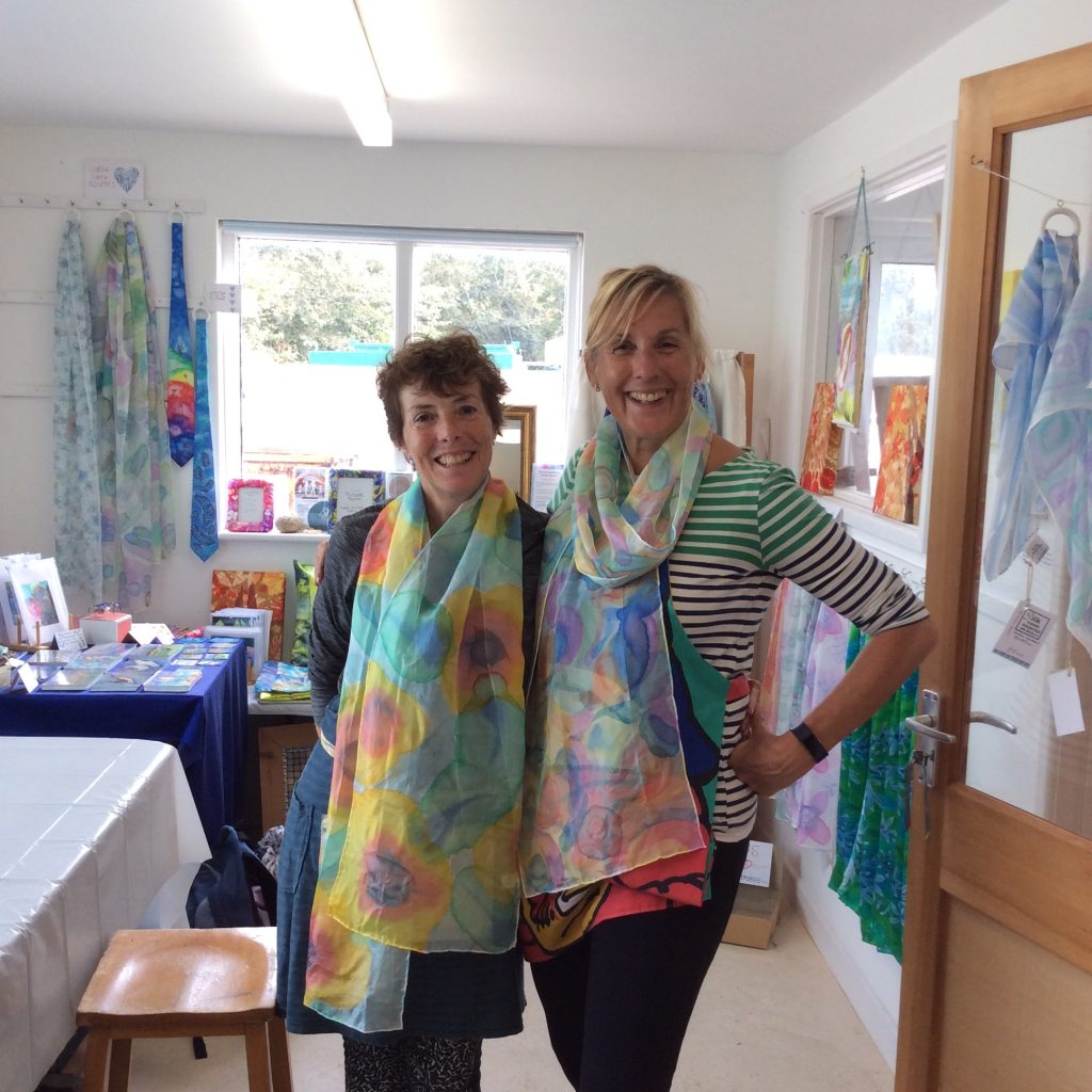 Two smiling women modelling their hand painted scarves